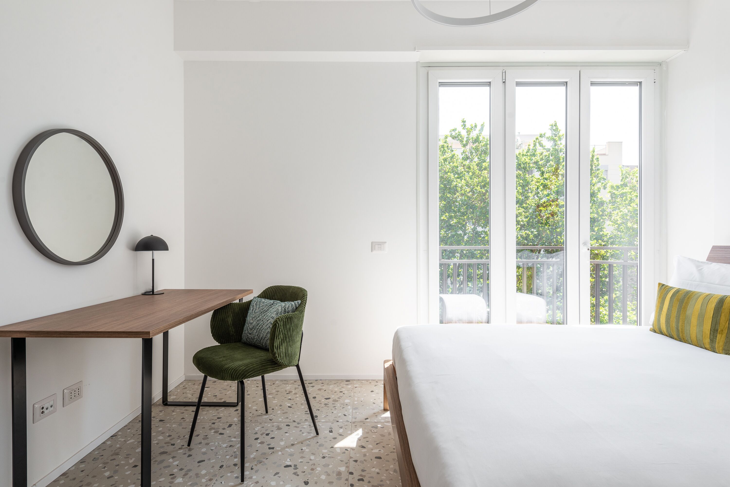 Une chambre à coucher comprenant un lit, un bureau, une chaise et une grande fenêtre donnant sur un balcon.