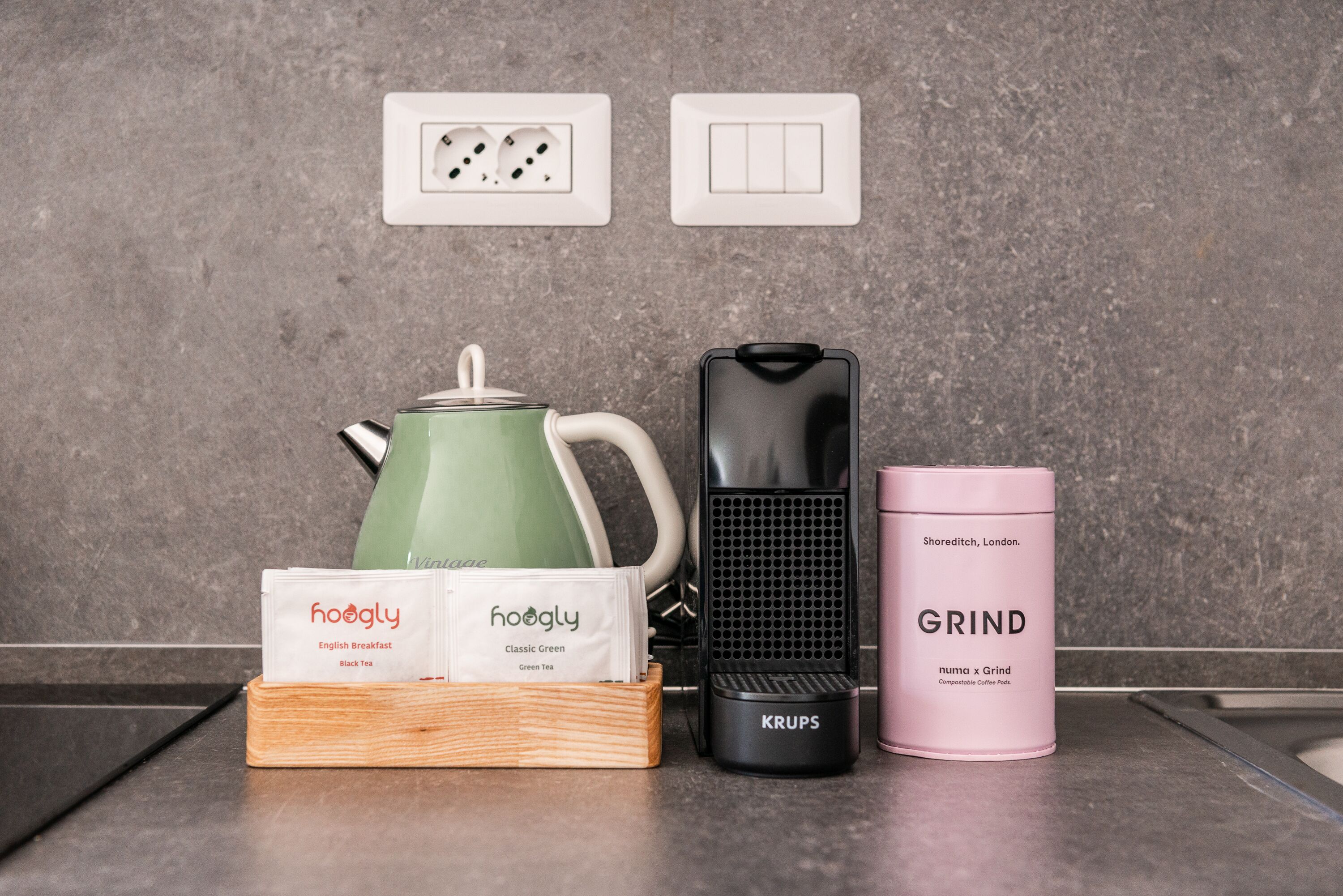 Un plan de travail de cuisine avec une bouilloire, une machine à café et un récipient pour les capsules de café.