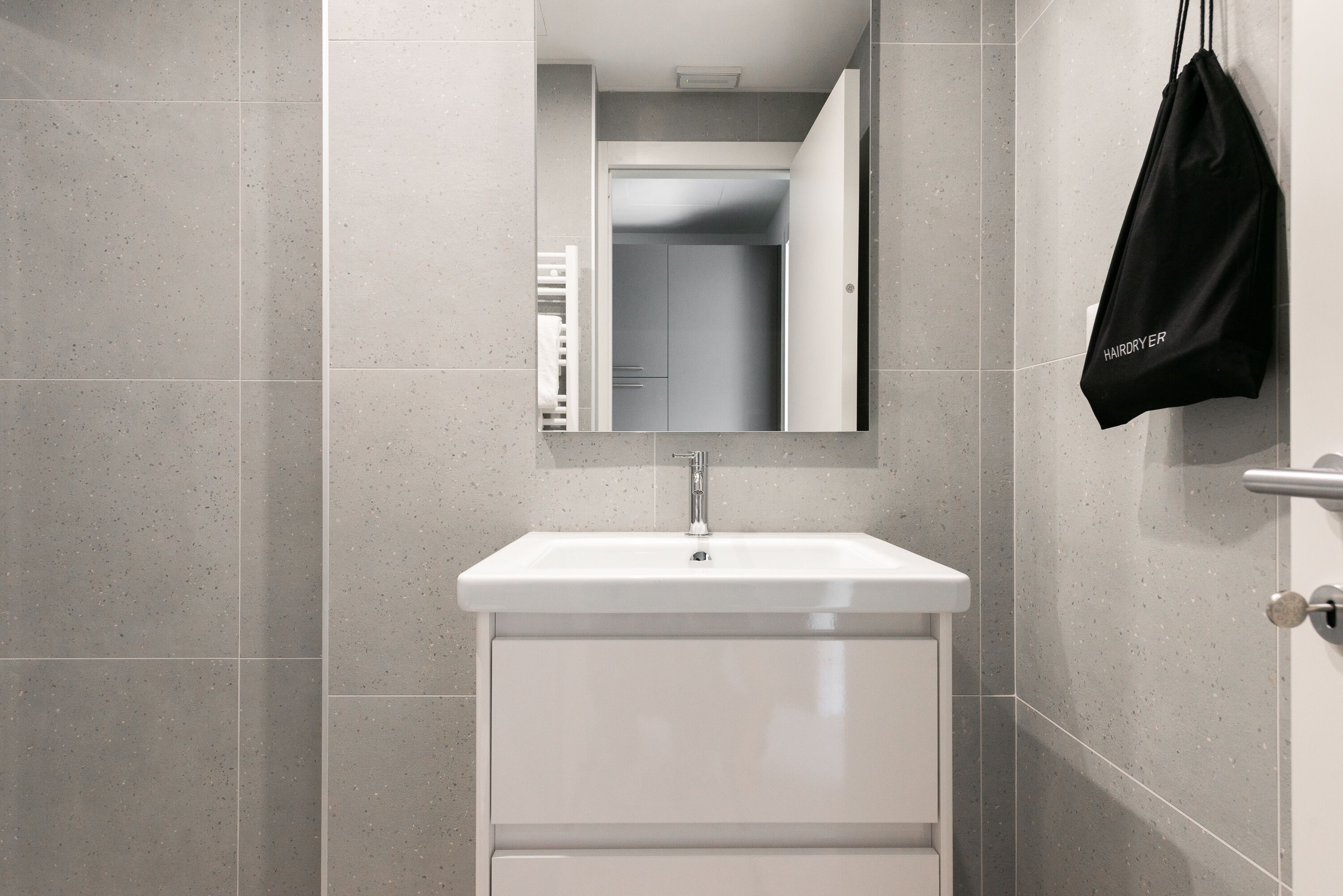 Ein Badezimmer mit einem weißen Waschbecken, einem Spiegel und einer schwarzen Tasche, die an der Wand hängt.