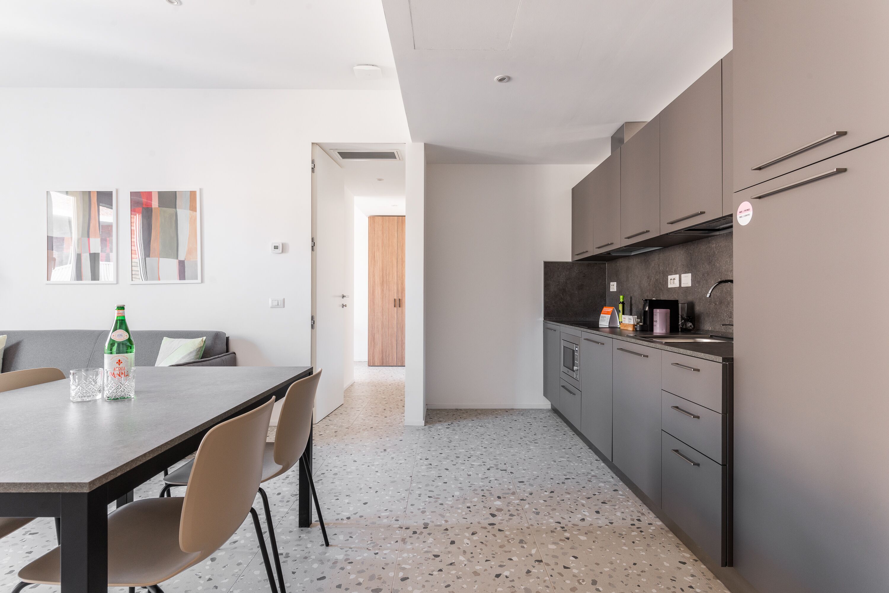 Una cocina moderna con armarios grises, un comedor con mesa y sillas, y un pasillo que conduce a una puerta de madera.