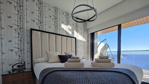 Un dormitorio moderno con una cama grande, un sillón colgante y vistas al mar.