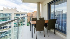 Un balcó amb taula i cadires, amb vista a un paisatge urbà amb edificis moderns.