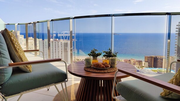 A balcony with a table set for breakfast, overlooking a beach and cityscape. - SUNSET WAVES fresh apartments (Benidorm)