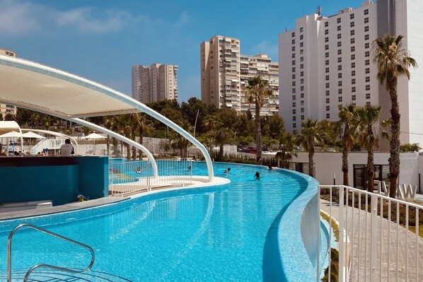 A swimming pool with a curved design, surrounded by palm trees and modern buildings in the background.