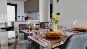 Un espace repas moderne avec une table en verre, de la verrerie transparente et un vase rempli de fleurs jaunes.