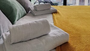 Une chambre d’hôtel avec un lit, des oreillers, une couverture jaune et une vue sur la mer, visible à travers de grandes fenêtres.