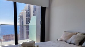 A bedroom with a large bed, two rolled towels, a view of a cityscape through a balcony, and a modern interior design. - SUNSET WAVES blue sky apartment (Benidorm)