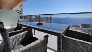 A balcony with a glass table and wicker chairs, overlooking a cityscape and the sea. - SUNSET WAVES blue sky apartment (Benidorm)
