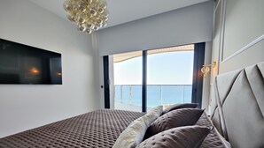 Ett sovrum med en stor säng, en tv som är monterad på väggen och en balkong med utsikt över havet.
