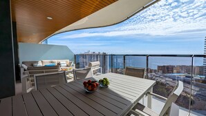 Un balcón con mesa de madera, asientos y vista panorámica de la ciudad.