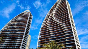 Dos edificios altos con varios balcones, probablemente apartamentos o habitaciones de hotel, bajo un cielo azul despejado.