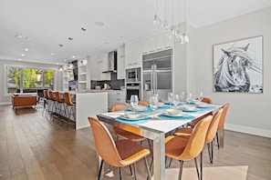 A modern kitchen with stainless steel appliances, a dining area with a large table set for six, and a large window providing natural light. - Downtown Luxury with Fast Wi-Fi & Amazing Kitchen! (Calgary)