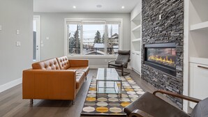 A modern living room with a stone fireplace, a leather sofa, a glass coffee table, and a view of the outside through large windows.