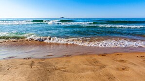 Una playa con agua azul cristalina, olas y una orilla arenosa.