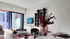 Un comedor moderno con una mesa de vidrio, individuales rojos y un jarrón con flores rojas.