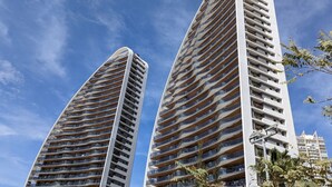 Dos edificios altos con múltiples balcones, probablemente unidades residenciales u habitaciones de hotel, bajo un cielo azul despejado.