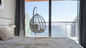 Un dormitorio con una cama grande, una silla colgante y vistas al mar.