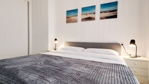 Een net opgemaakt bed met een geruite deken, een nachtkastje met een lamp, en twee ingelijste foto's aan de muur.
