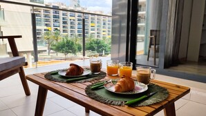 Een ontbijttafel met croissants, koffie en sinaasappelsap op een balkon met uitzicht op de stad.