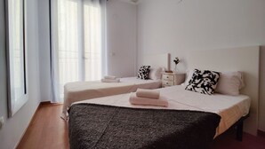Une chambre d’hôtel avec deux lits, une grande fenêtre avec des rideaux, une table de chevet avec une lampe et un plaid de couleur sombre sur le lit.