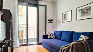 Un salon moderne avec un canapé bleu, un téléviseur à écran plat et une porte-fenêtre coulissante donnant sur un balcon.