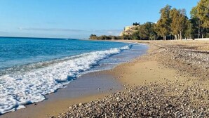 Ein Strand mit Kieselsteinen, einem klaren blauen Meer und einem Gebäude im Hintergrund.