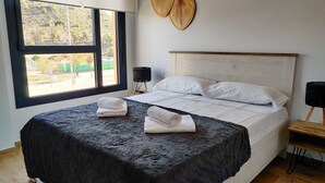 Ein Schlafzimmer mit einem großen Bett, zwei weißen Kissen, einer schwarzen, flauschigen Decke und einem Fenster mit Blick auf Bäume und ein Gebäude.