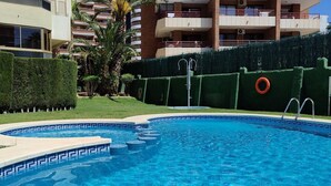A swimming pool with a geometric tile pattern, surrounded by a well-maintained hedge and a palm tree. - GERONA sea view apartments (Benidorm)