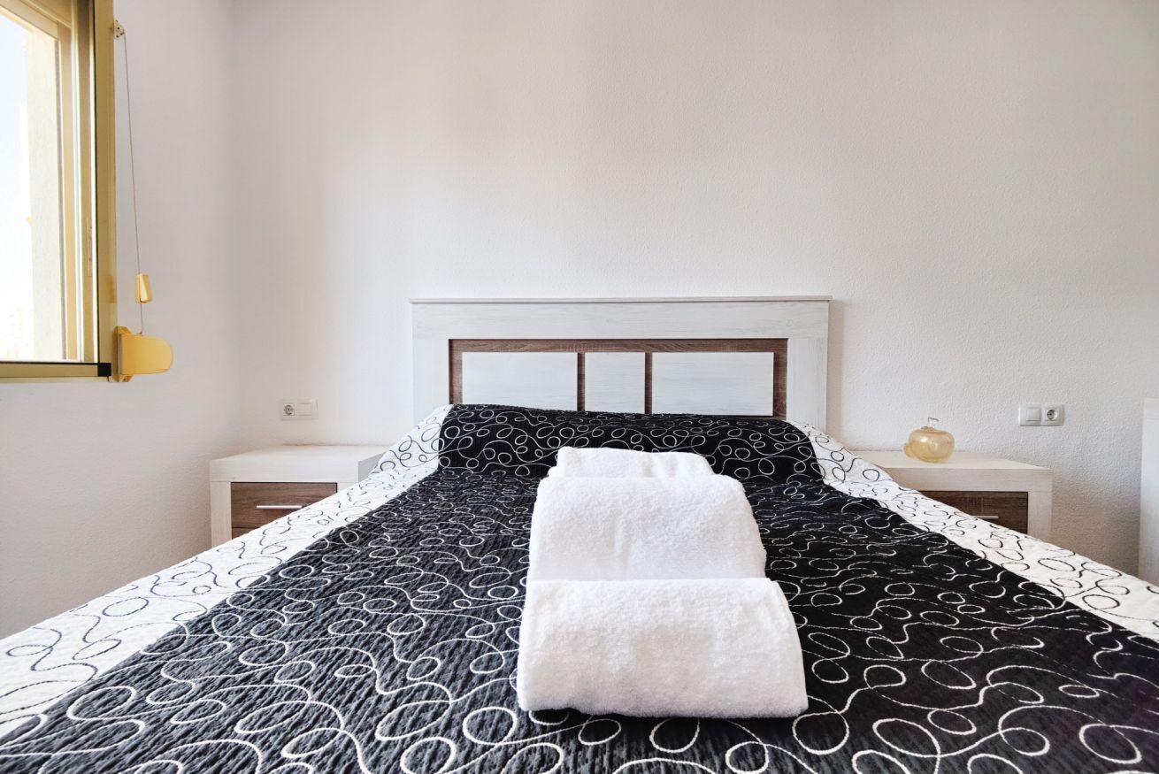Un lit bien fait, recouvert d’une couvre-lit à motifs, avec deux serviettes blanches pliées posées dessus.