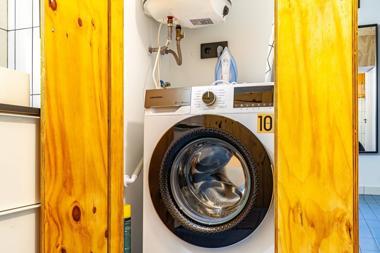 Eine Waschmaschine ist von vorne zu sehen, mit Bedienfeld, Wasseranschluss und Ablaufschlauch.