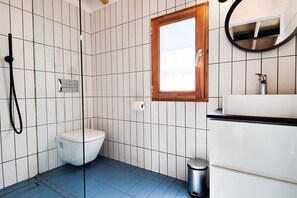Une salle de bain avec des toilettes blanches, une douche, un lavabo et un miroir.