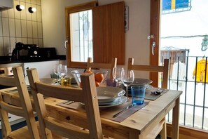 Une table de salle à manger en bois, mise avec des assiettes, des verres et des couverts, près d’une fenêtre donnant sur l’extérieur.