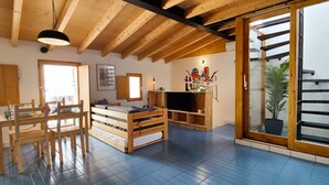 Een knus ingerichte kamer met houten plafond, een bed, een televisie en een schuifdeur naar een balkon.