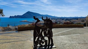 Een metalen sculptuur van twee figuren met hoorns, een fiets, en een berg op de achtergrond.