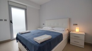 Um quarto com uma cama, uma mesa de cabeceira com abajur e uma porta.
