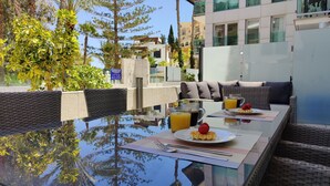 A dining area with a glass table, wicker furniture, and a view of buildings and trees. - MIRADOR beach apartments (Benidorm)