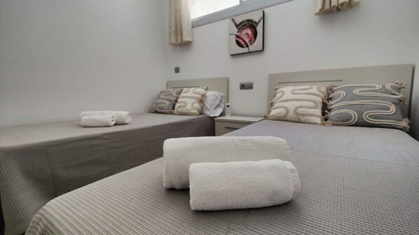 Habitación de hotel con dos camas, cada una con una colcha gris y almohadas a juego. Hay toallas sobre las camas y un cuadro en la pared.