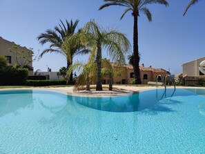 A clear blue swimming pool surrounded by palm trees and a building with a tiled roof. - MIRADOR vacation home (Golf Badia)