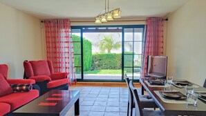 Een woonkamer met een bank, salontafel, televisie en een eethoek met stoelen en een tafel gedekt voor twee personen.