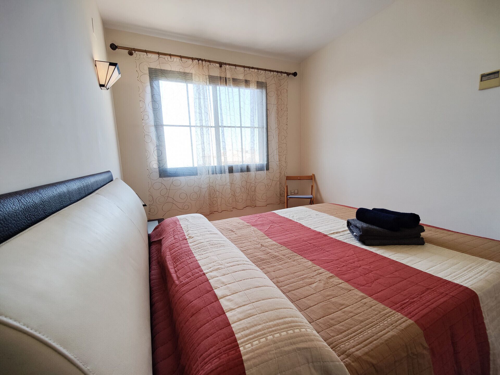 Une pièce simple et épurée, avec un lit, une chaise et une fenêtre avec des rideaux.