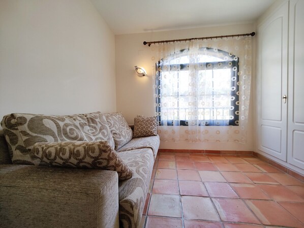 A living room with a sofa, a window with patterned curtains, and a tiled floor. - MIRADOR vacation home (Golf Badia)