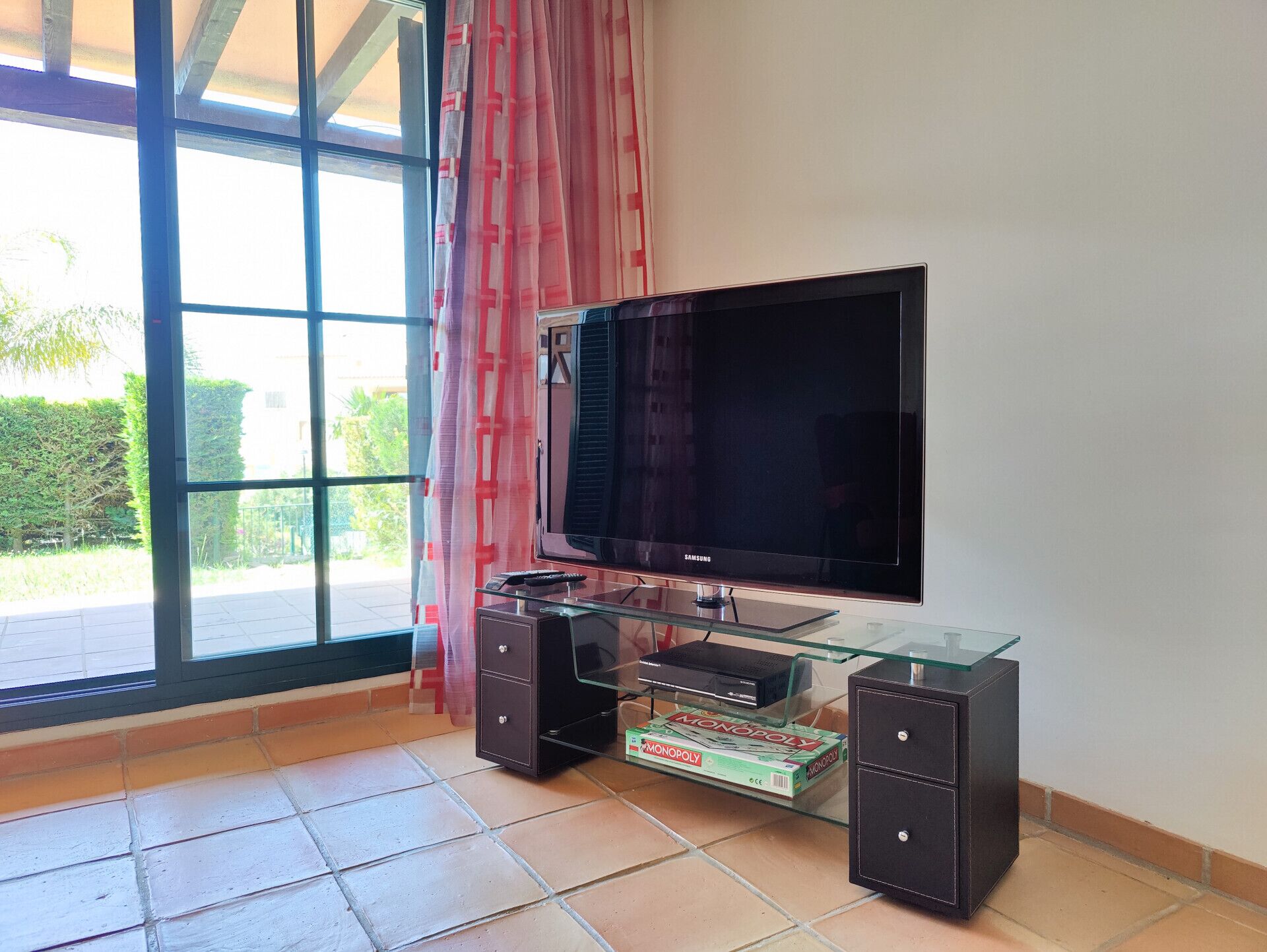 Una sala de estar con un televisor de pantalla plana grande sobre un mueble de vidrio, un juego de mesa Monopoly y un armario.