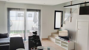 Un salon moderne comprenant un coin repas, un escalier et un téléviseur fixé au mur.