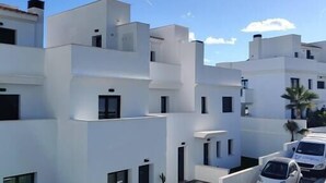 Un bâtiment moderne, blanc, doté d’un toit plat et de nombreuses fenêtres. On peut voir des voitures garées devant et un petit arbre au premier plan.