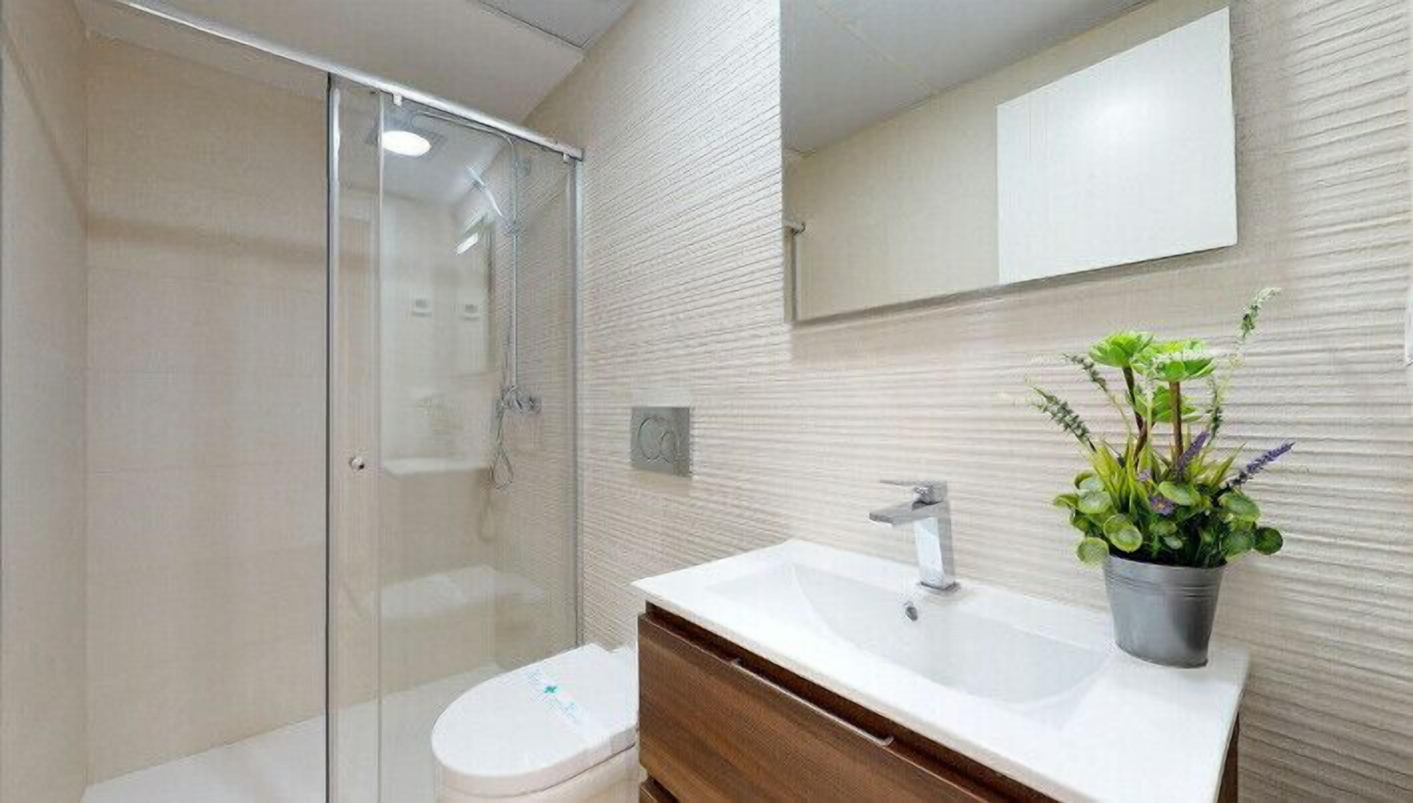 A modern bathroom with a glass shower enclosure, a white sink with a plant, and a large mirror.