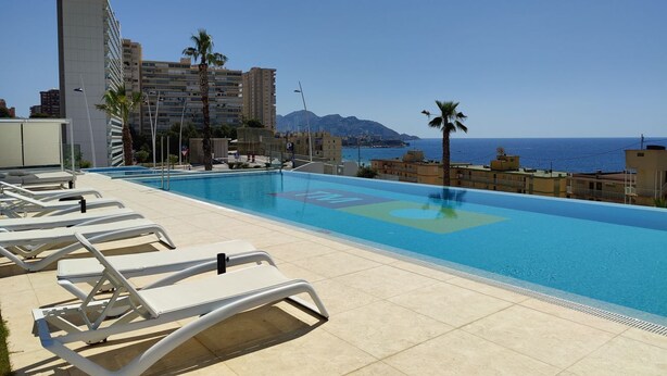 A swimming pool with lounge chairs, a clear view of the sea, and a mountain in the background. - SUNSET CLIFFS sea & sky apartments (Benidorm)