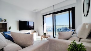 A modern living room with a flat-screen TV, a sofa set, a small round table, and a balcony with a view. - SUNSET CLIFFS sea & sky apartments (Benidorm)