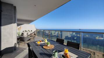 A balcony with a table set for breakfast, overlooking a cityscape and the sea.