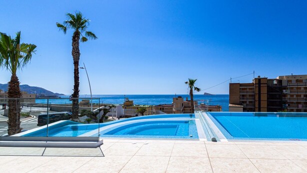 A swimming pool with clear blue water, surrounded by palm trees and a view of the sea. - SUNSET CLIFFS sea view apartments (Benidorm)