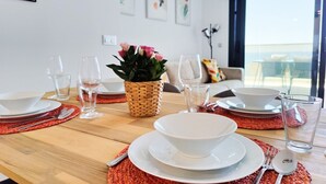 A dining table set with white plates, bowls, and cutlery, a woven basket with flowers, and a view of the outdoors through a large window. - SUNSET CLIFFS sea view apartments (Benidorm)